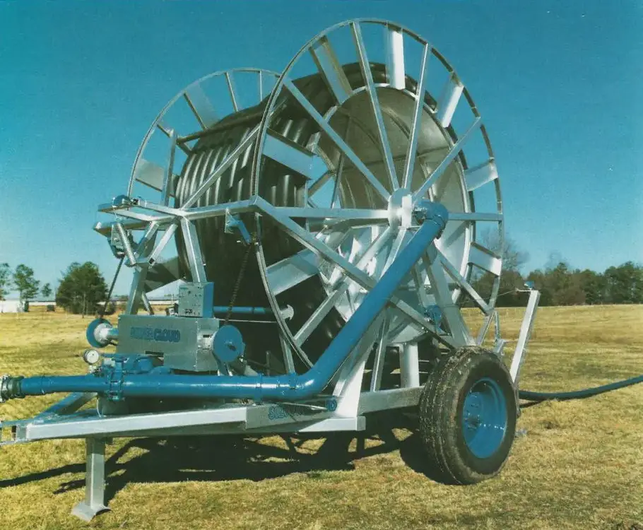 A large, blue and silver mechanical irrigation wheel on a grassy field under a clear sky.